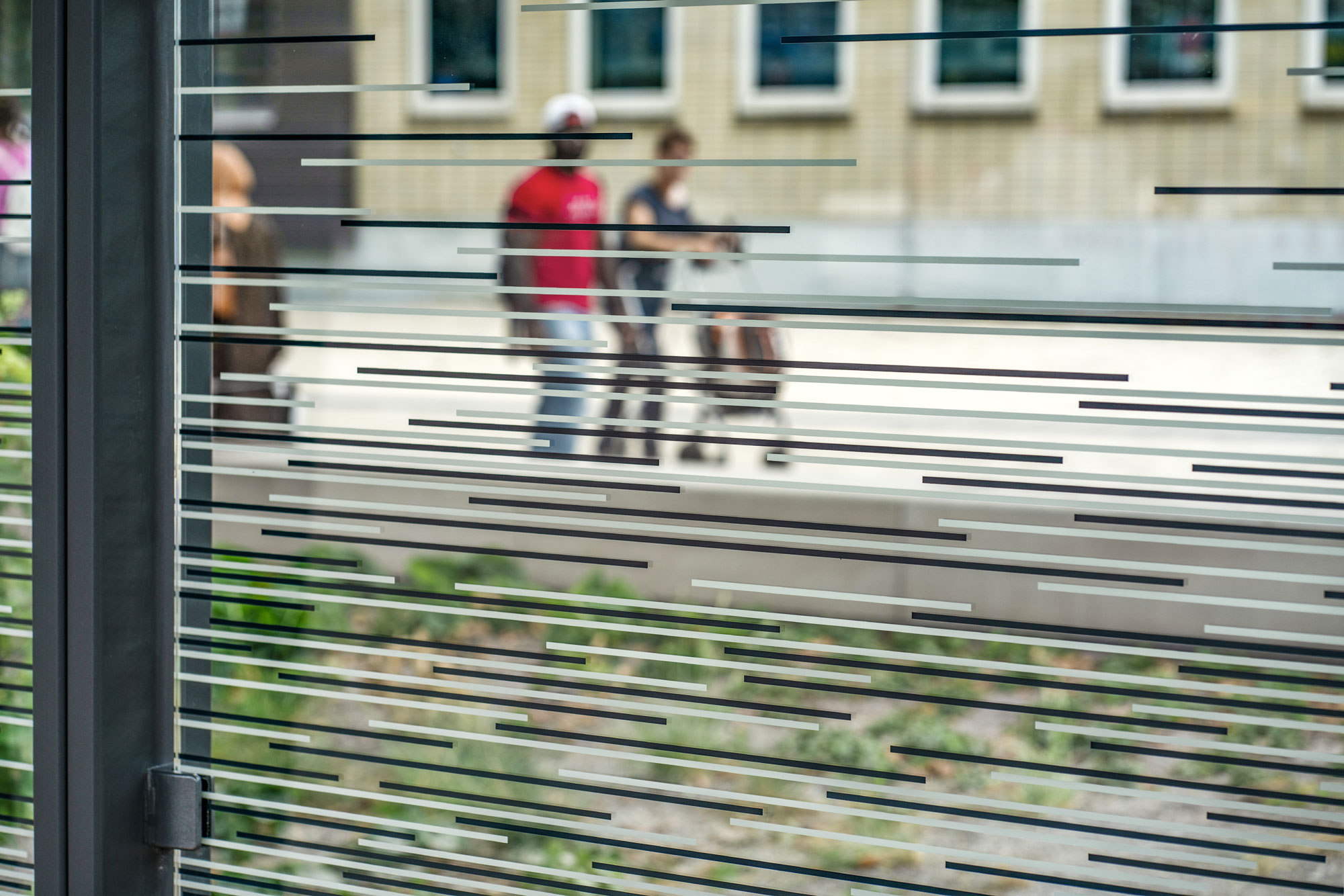 Glasscheibe mit Durchlaufschutz dahinter laufen Menschen